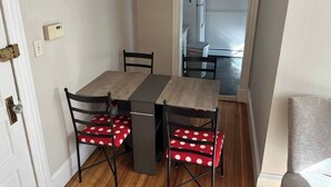 A dining area with a table and four chairs, a door with a handle, and a view into a kitchen area with a refrigerator and microwave. - 5 Min to Salem~Comfy King Beds (Beverly)