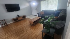 A living room with a flat-screen TV mounted on the wall, a dark-colored sofa with cushions, a wooden coffee table, and a potted plant. - Tampa Travel Hub - TPA Airport tranquility (Tampa)