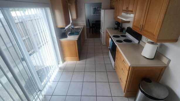 A compact kitchen with wooden cabinets, a stove, and a sink. - Tampa Travel Hub - TPA Airport tranquility (Tampa)