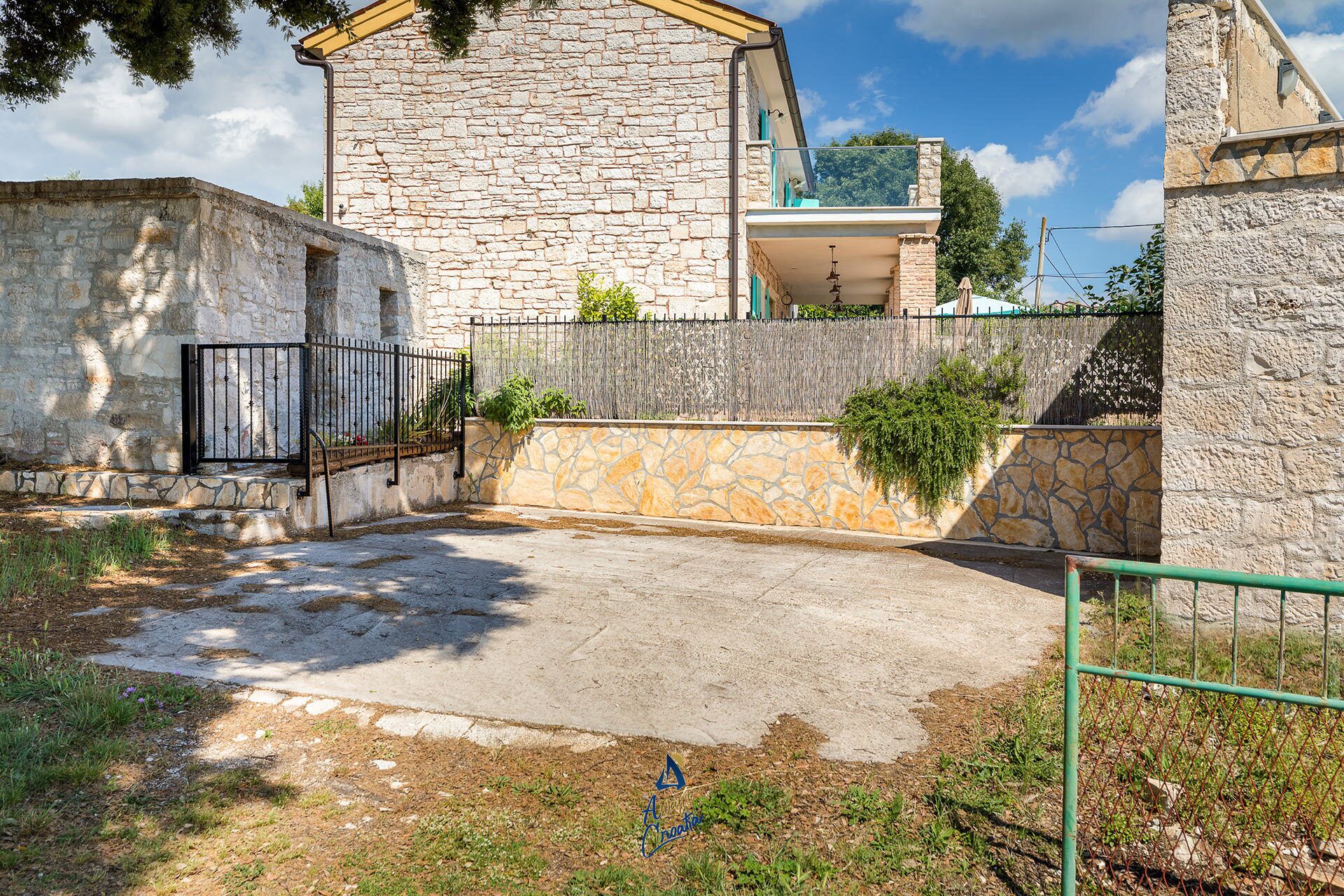 A courtyard with stone walls, a metal gate, and a paved area.