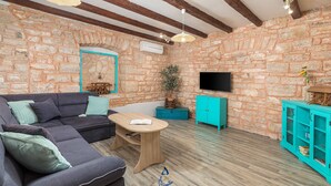 Ein gemütliches Wohnzimmer mit Steinwand, grauem Sofa, Holztisch und einem türkisfarbenen Schrank.