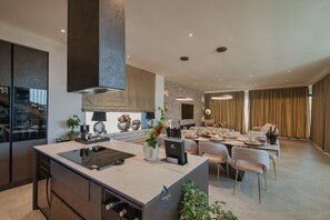 Una cocina moderna con una isla central, zona de comedor con sofá y sillas, y sala de estar con un ventanal grande.