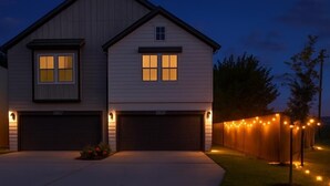 A two-story house with a garage, a small porch, and a well-lit driveway.