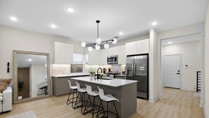 A modern kitchen with a central island, bar stools, a microwave, and a refrigerator.