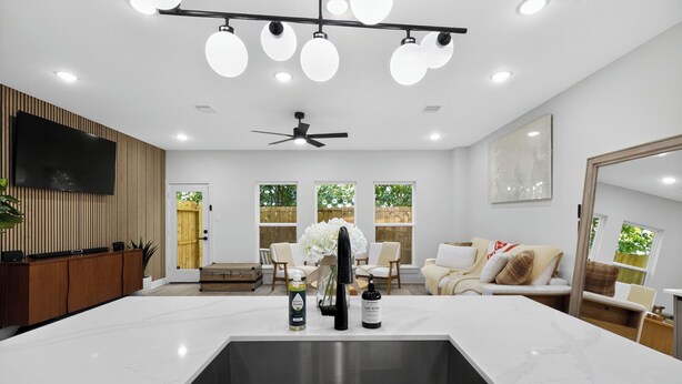 A modern kitchen with a large island, recessed ceiling lights, a flat-screen TV, and a ceiling fan.