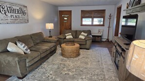Ein Wohnzimmer mit zwei Sofas, einem Couchtisch, einer Lampe, einem Fernseher und einem Schild mit der Aufschrift 'Gathering Place'.