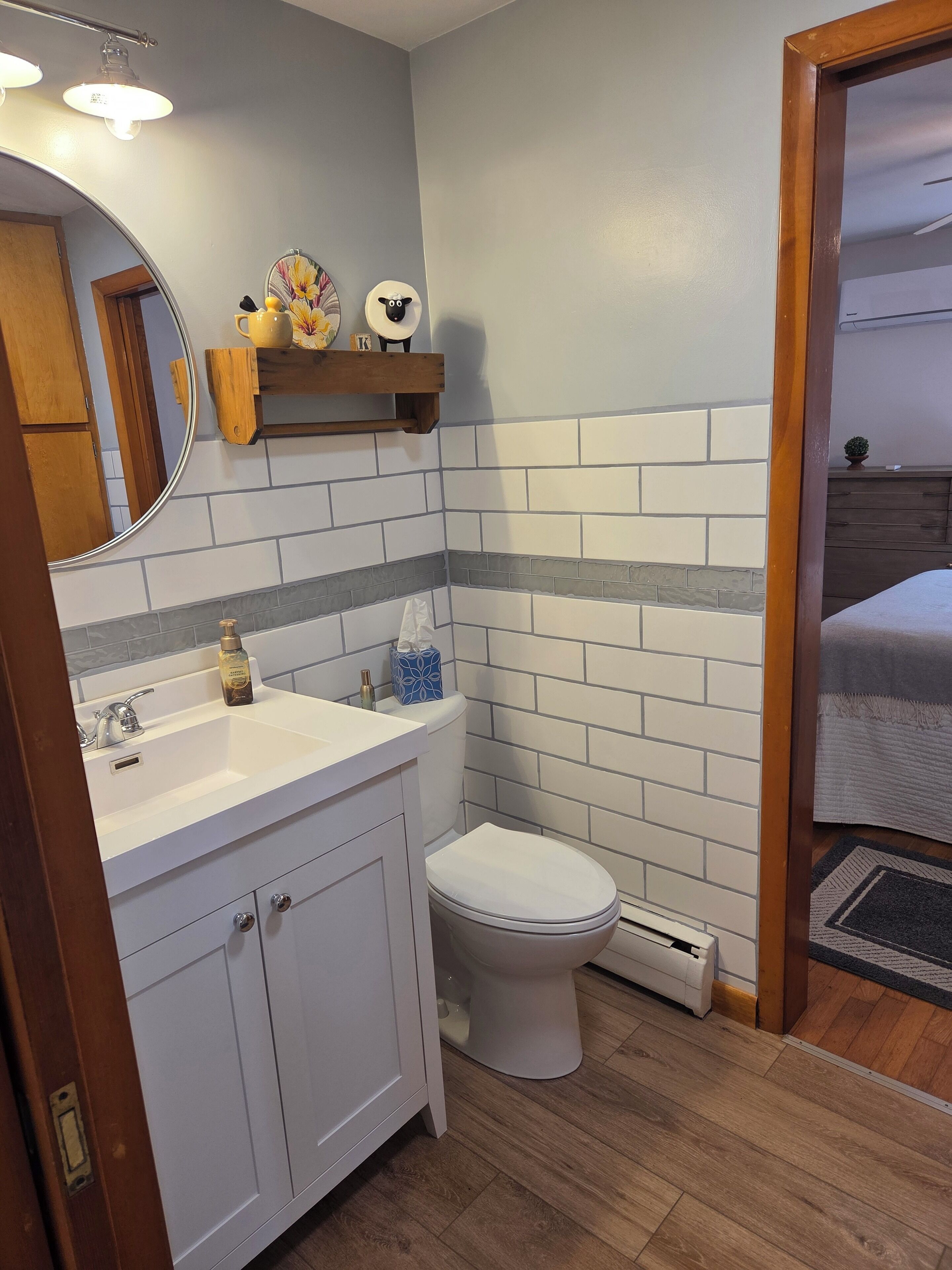 A bathroom with a white sink, a toilet, and a mirror. There are decorative items on a shelf above the mirror.
