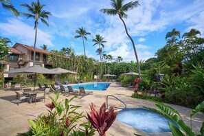 A pool area with lounge chairs, umbrellas, and a hot tub.