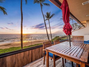 Eine Holzterrasse mit Tisch und Stühlen, mit Blick auf einen Strand mit Palmen und dem Meer.