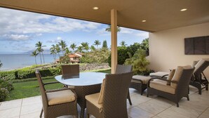 Une terrasse couverte avec une table ronde et des chaises en osier, offrant une vue panoramique sur l’océan et les palmiers.