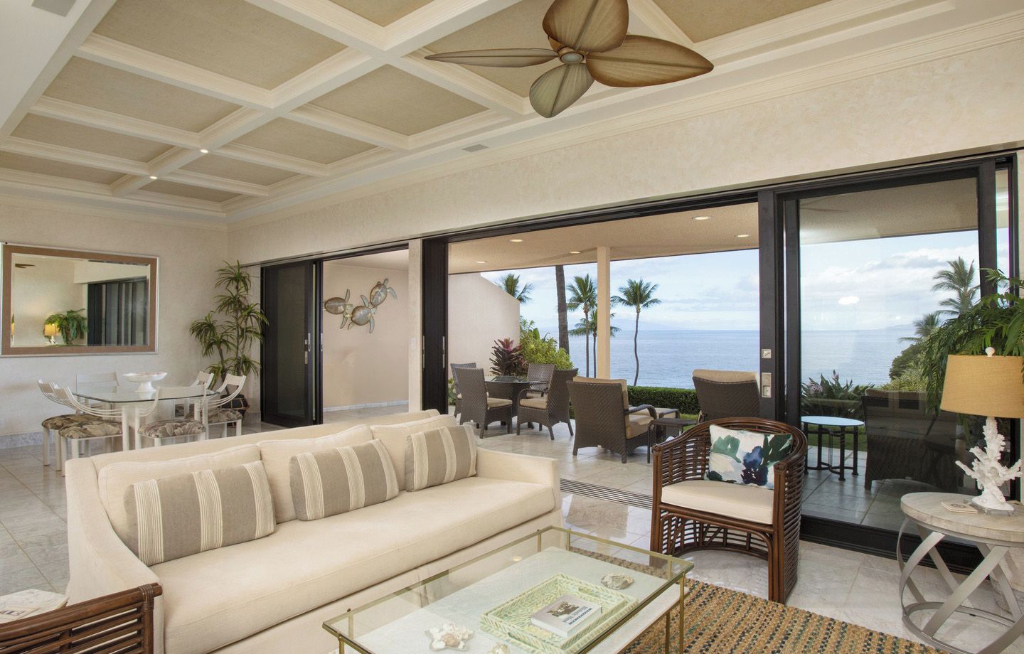 A spacious living area with a sofa, chairs, a glass coffee table, and a view of the ocean.