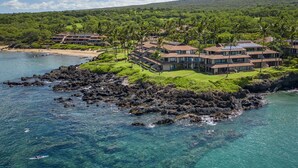 Un complejo turístico en la costa con varias edificaciones, un litoral rocoso y aguas azules cristalinas.