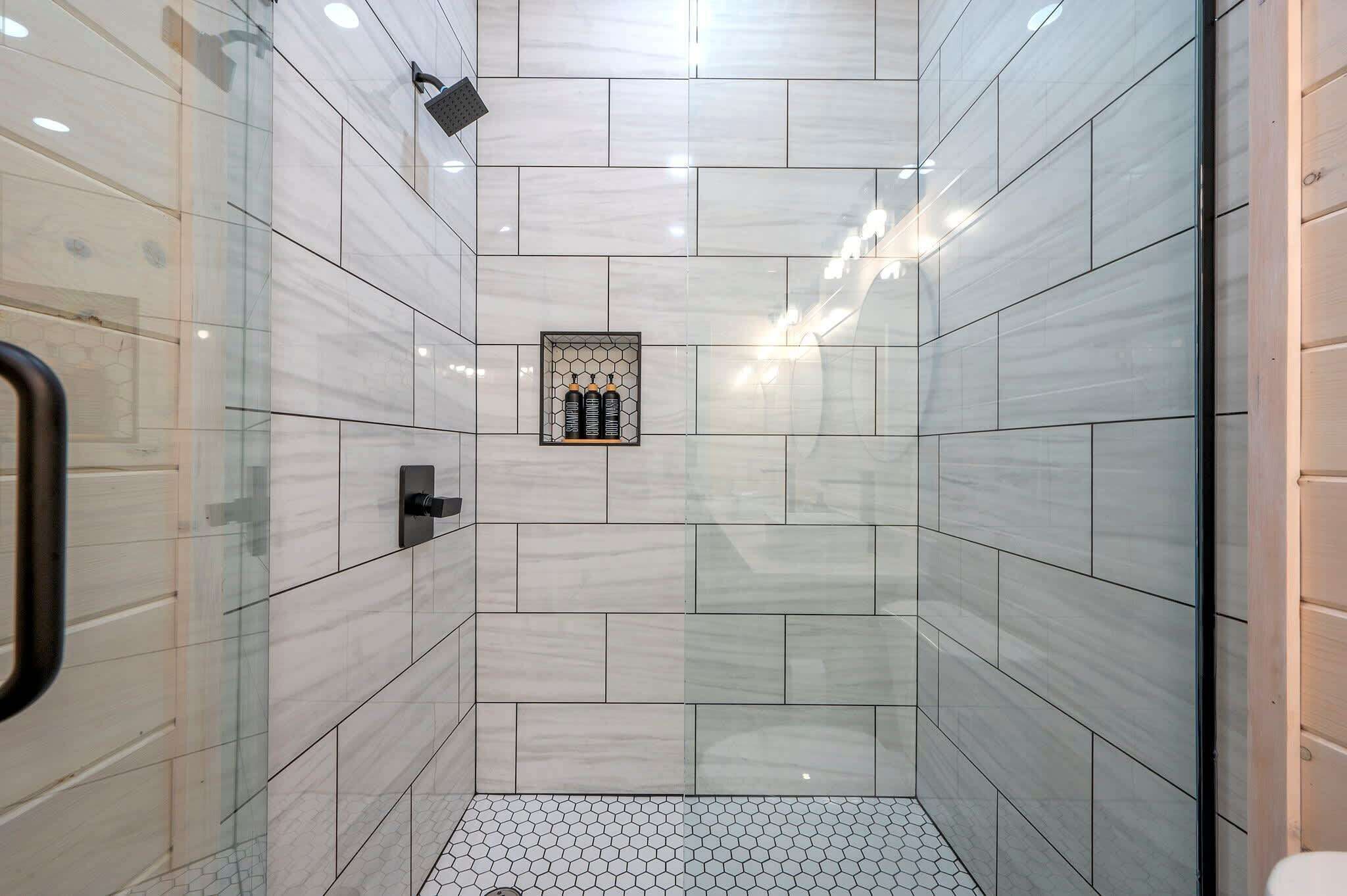 A modern bathroom with large tiled walls, a glass shower enclosure, and a hexagonal tile floor.
