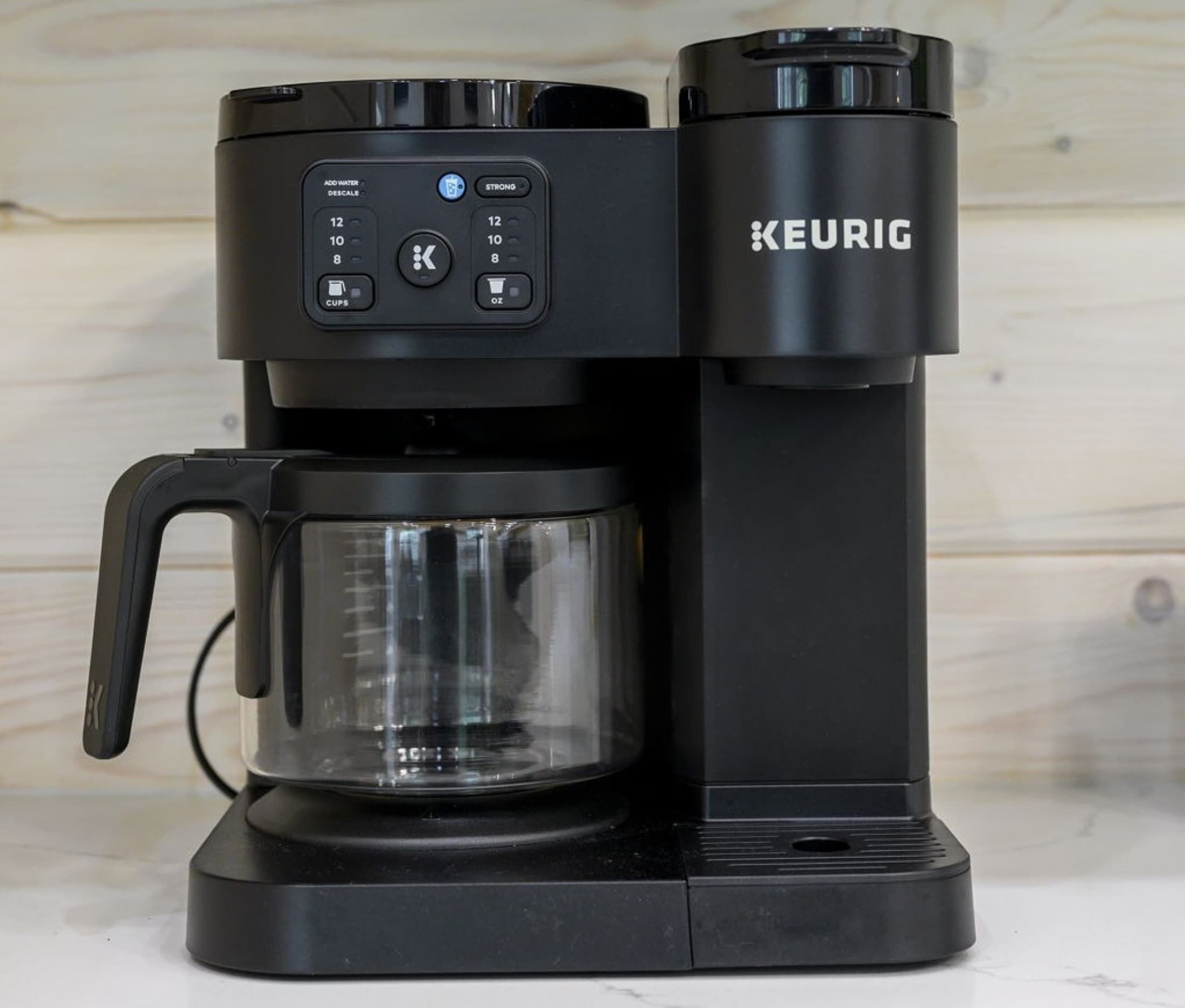 Een Keurig koffiezetapparaat met een glazen kan en een zwart voetstuk.