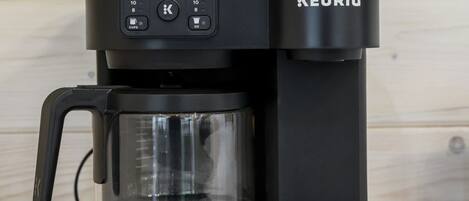 Een Keurig koffiezetapparaat met een glazen kan en een zwart voetstuk.