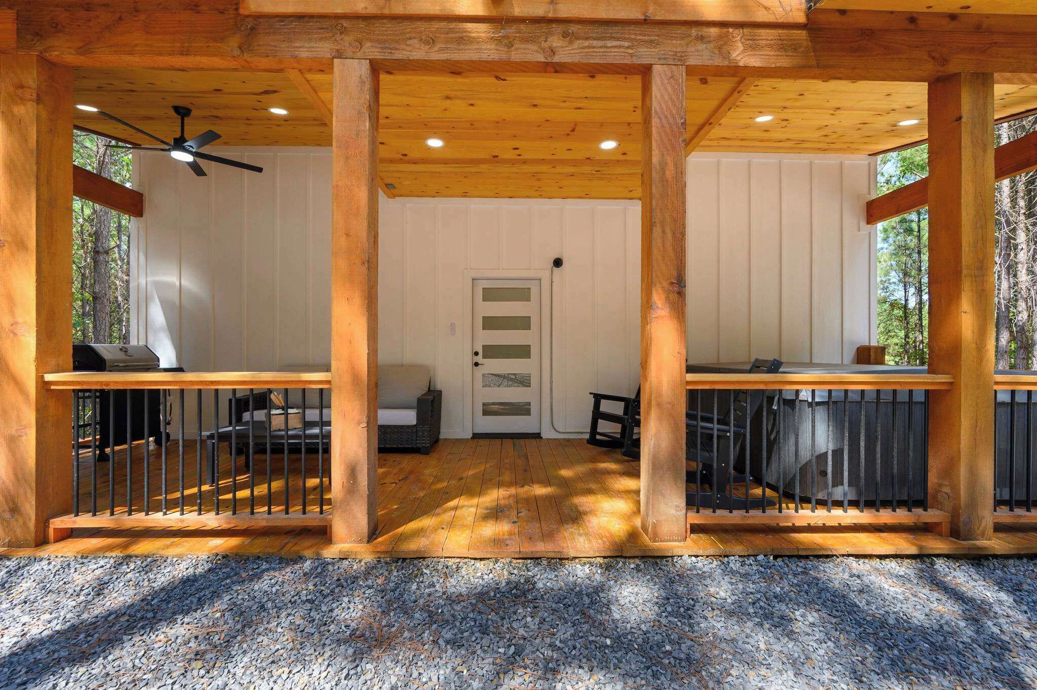 A covered outdoor area with a wooden deck, a ceiling fan, and a door leading to an interior space.