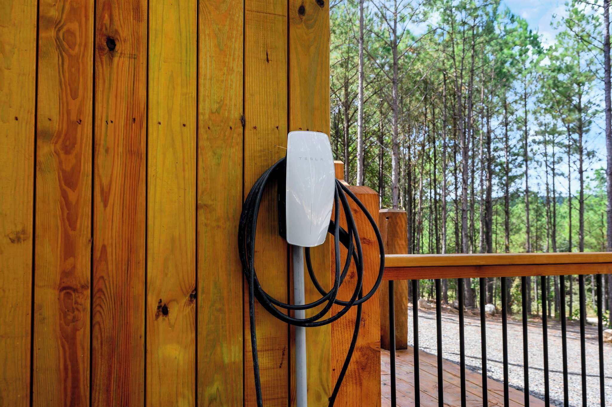 Una estación de carga Tesla fijada en una pared de madera, con vistas a un área boscosa.