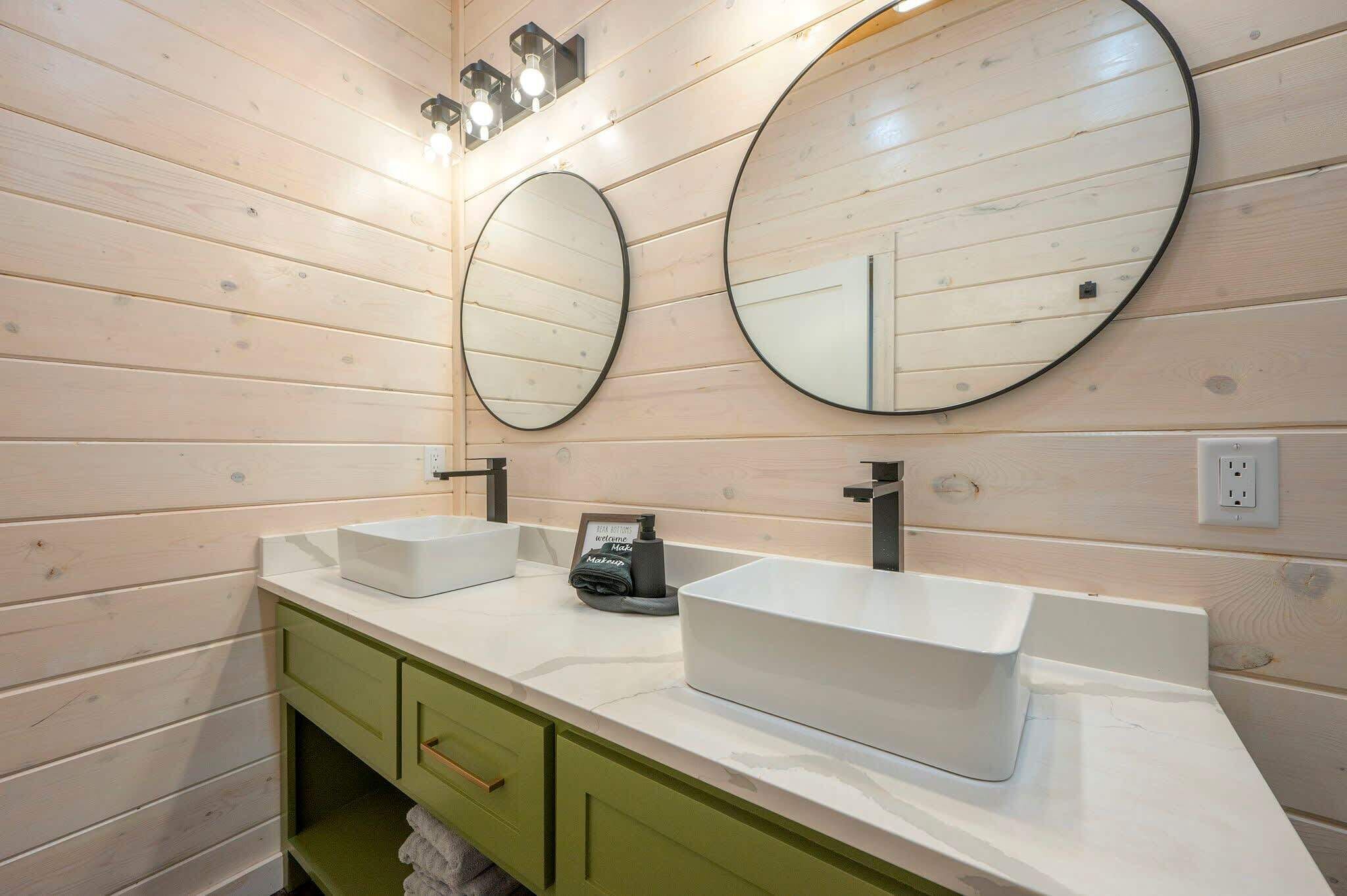 A bathroom with two sinks, green cabinets, and two round mirrors.