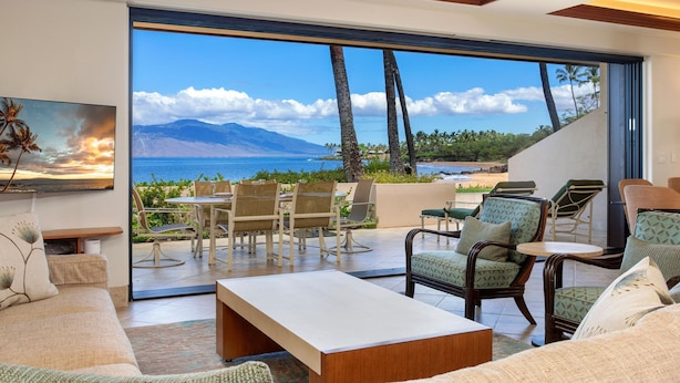 Ein großzügiger Wohnbereich mit einer großen Schiebeglastür, die auf einen Balkon mit Blick auf Strand und Berge führt.