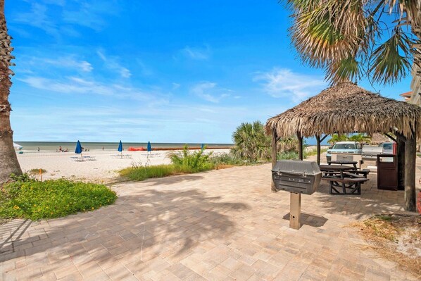 Une terrasse au bord de la plage, avec un espace barbecue, des parasols et une vue sur la plage.