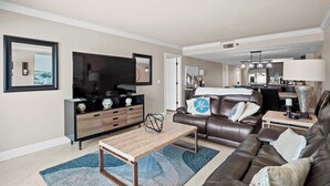 Ein modernes Wohnzimmer mit Flachbildfernseher, Couchtisch aus Holz, Ledersofa und Essbereich mit Tisch und Stühlen.