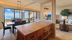 A spacious living area with a large wooden island, a dining area with a view of the ocean, and a cozy seating area with a lamp and plant. - 2nd Floor Ocean Views | Epic Sunsets | Makena Surf F208 (Wailea)