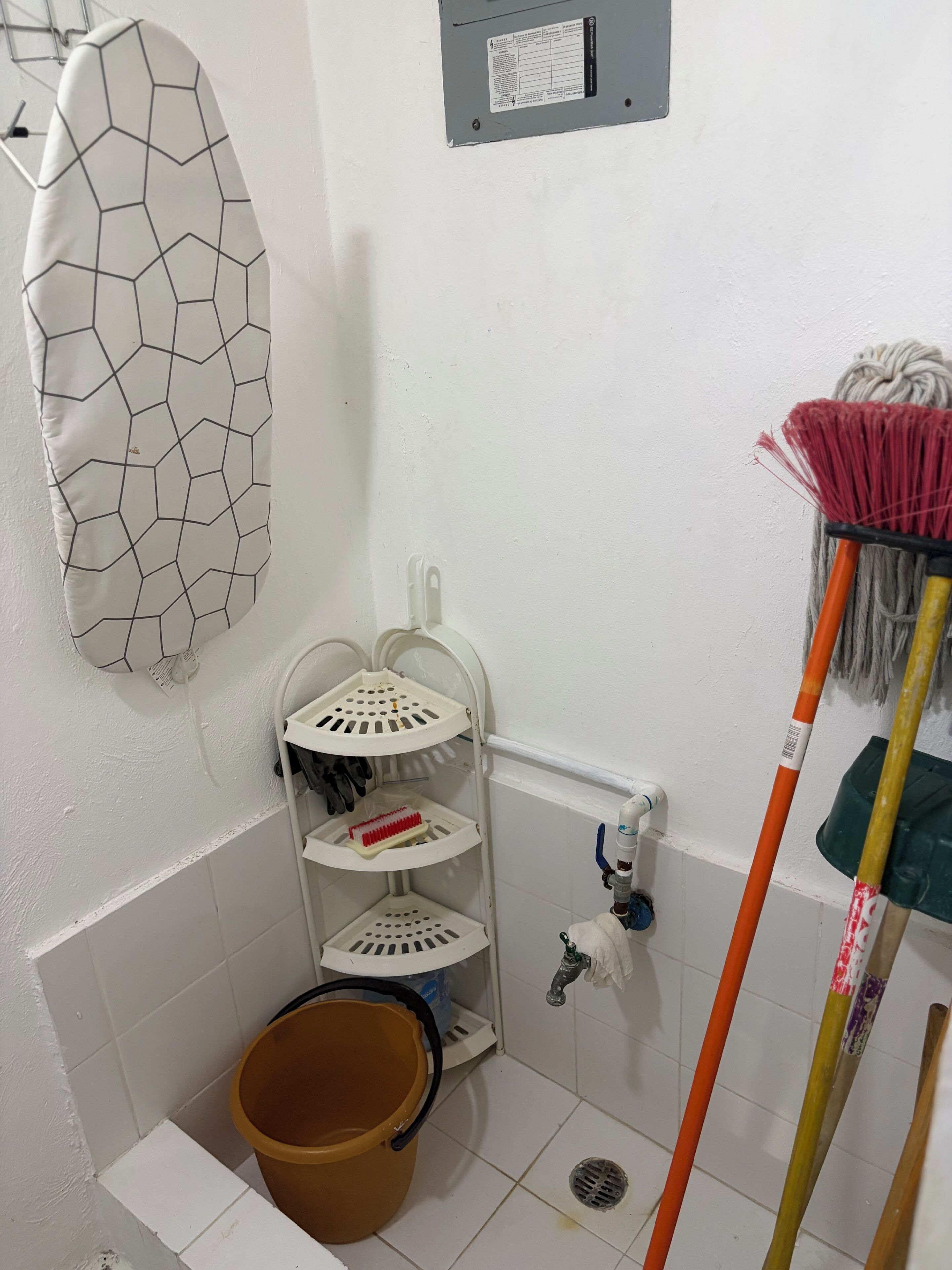 A bathroom with a white tiled floor, a corner shelf with cleaning supplies, a mop, and a bucket.