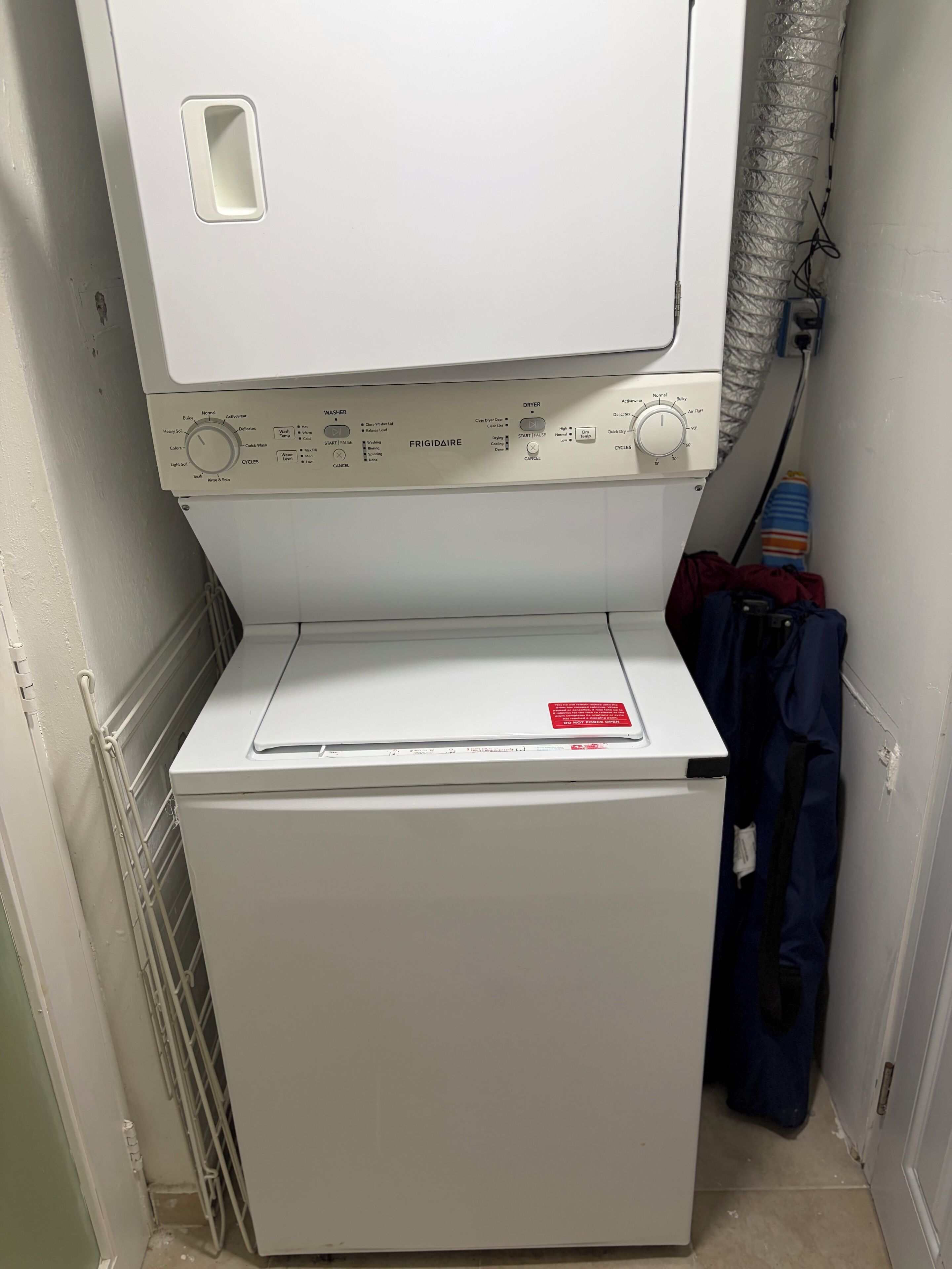 A compact, white front-loading washer and dryer unit with a control panel featuring multiple settings and a red safety label.