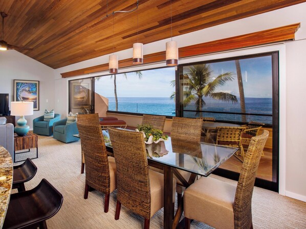 A modern living room with a glass table, wicker chairs, and a view of the ocean.