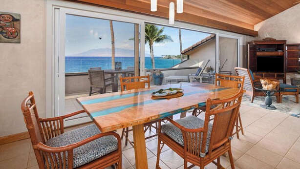 A dining area with a large table, chairs, and a view of the ocean.
