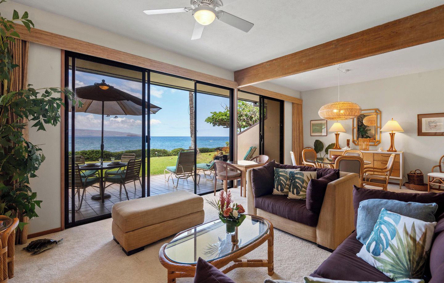 A spacious living area with a large sliding glass door leading to a balcony overlooking the ocean, furnished with a sofa, armchairs, and a coffee table.