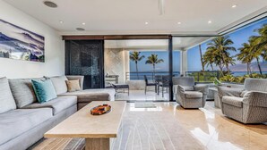 Een moderne woonkamer met een bank, stoelen, een salontafel en uitzicht op de oceaan door grote ramen.