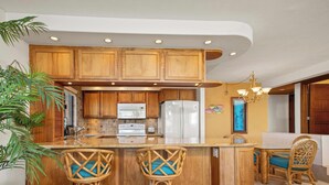 A kitchen with wooden cabinets, a central island with stools, and a dining area with wicker chairs.