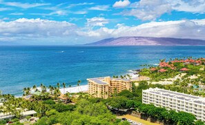 Un complejo turístico frente al mar, con varias construcciones, una playa y una montaña al fondo.