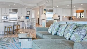 A modern living room with a grey sofa, a glass coffee table, and a blue patterned rug.