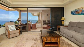 A spacious living room with a view of the ocean, a balcony with wicker furniture, and a modern ceiling fan. - Polo Beach Club 801 | 8th Floor Ocean Views, Beachfront Pool & Beach Access (Wailea)