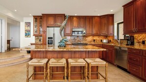 A spacious kitchen with wooden cabinets, granite countertops, a stainless steel refrigerator, and a built-in oven. - Polo Beach Club 801 | 8th Floor Ocean Views, Beachfront Pool & Beach Access (Wailea)