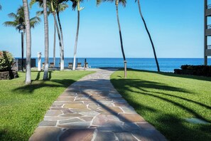 A stone pathway leading to a beachside area with palm trees and a view of the ocean. - Polo Beach Club 801 | 8th Floor Ocean Views, Beachfront Pool & Beach Access (Wailea)