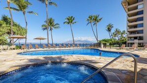A pool area with lounge chairs, palm trees, and a building with balconies. - Polo Beach Club 801 | 8th Floor Ocean Views, Beachfront Pool & Beach Access (Wailea)