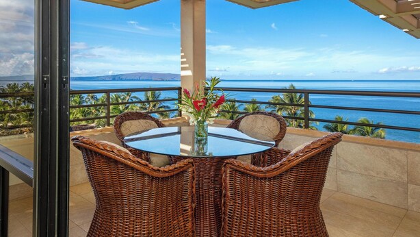 A balcony with wicker chairs and a glass table, overlooking a scenic ocean view. - Polo Beach Club 801 | 8th Floor Ocean Views, Beachfront Pool & Beach Access (Wailea)