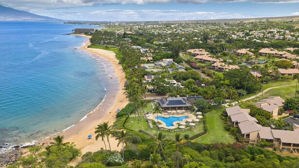Luftaufnahme eines Küstenresorts mit Strand, Schwimmbad und üppiger Vegetation.