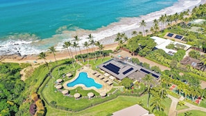 An aerial view of a resort with a swimming pool, beach access, and lush landscaping.