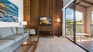 Un salon moderne avec un canapé, un téléviseur, un meuble en bois et un balcon aménagé avec du mobilier d’extérieur.