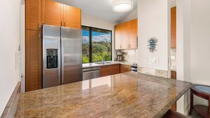 Une cuisine moderne dotée de meubles en bois, d’appareils électroménagers en acier inoxydable, de plans de travail en granit et de luminaires suspendus.