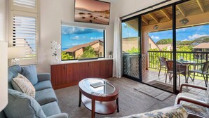 Un salon comprenant un canapé, une table basse et une grande fenêtre donnant sur une plage et des maisons.
