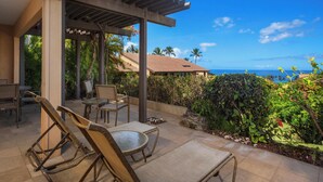 A covered outdoor seating area with chairs and tables, overlooking a lush garden and a view of the ocean.
