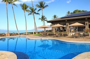 A pool area with lounge chairs and umbrellas, surrounded by palm trees and a view of the ocean.