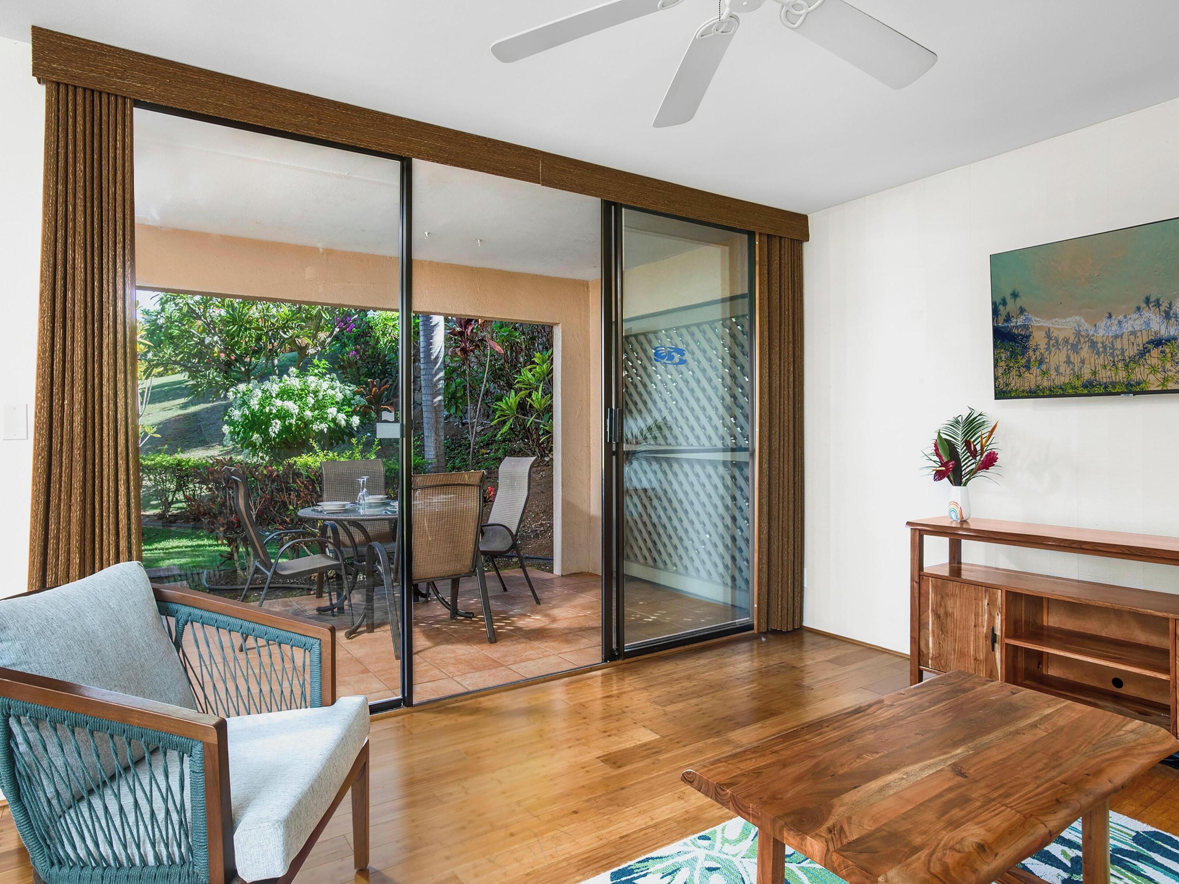 Une pièce spacieuse avec une table à manger en bois, un canapé et une vue sur un jardin, accessible par une porte-fenêtre coulissante.