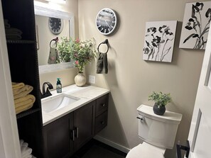 A bathroom with a sink, mirror, clock, toilet, and two wall-mounted flower paintings.