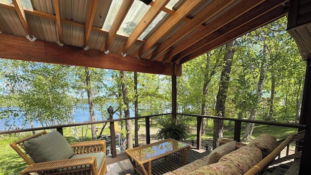 Une terrasse dotée de meubles en osier, d’une table en verre et offrant une vue sur le lac.